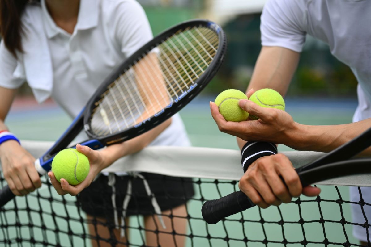 two people leaning on tennis net with tennis balls in their hands